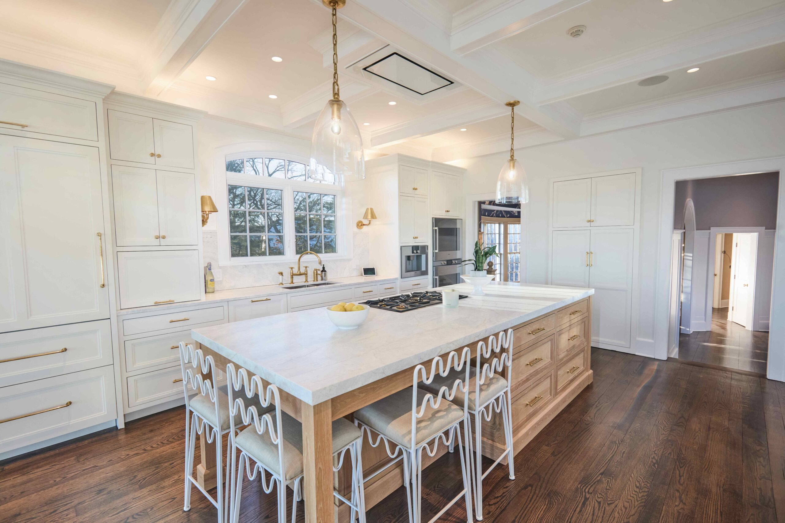 A spacious, bright kitchen with a large island, pendant lights, white cabinets, and gold fixtures.