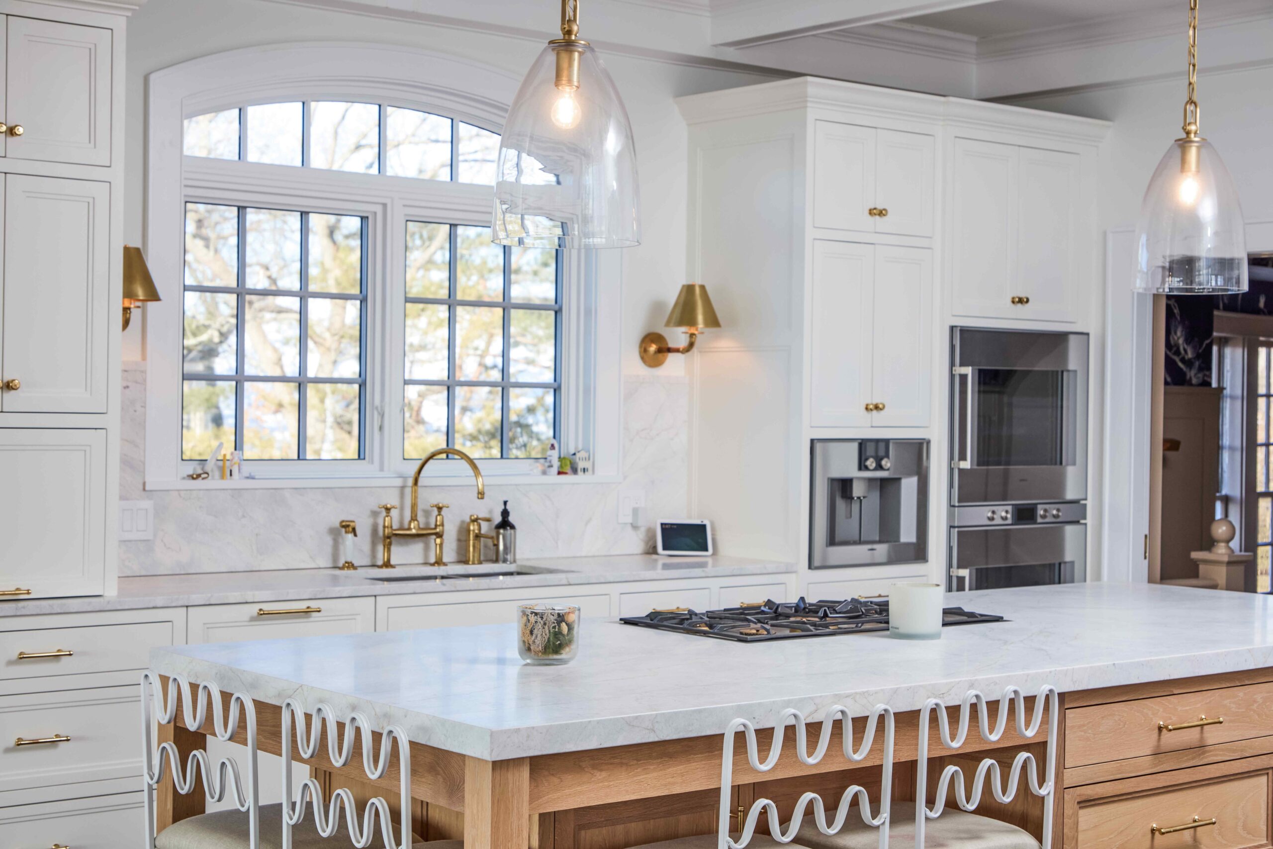 A contemporary kitchen featuring a large island, gold hardware, white cabinets, and an arched window.